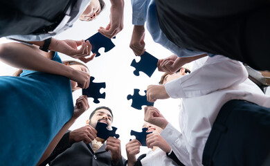 Below view of diverse corporate officer workers collaborate in office connecting puzzle pieces as...