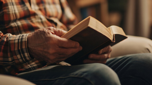 Close up of senior man reading book while sitting in vintage chair at home