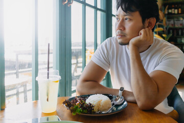Asian man in white t-shirt is waiting for someone to meet at the restaurant with Thai food stir fried pork with rice.