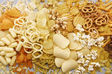 Colorful mix of salty snacks for beer varieties: chips and pretzels, onion rings and crackers. Non-healthy junk food background