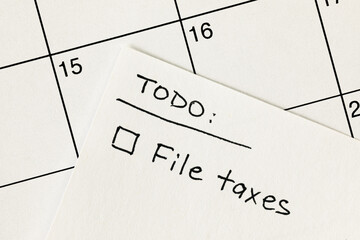 Hand written to-do list with 'File taxes' reminder written on a sticky note over a calendar, with income tax return filing deadline of April 15 - obrazy, fototapety, plakaty