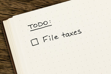 To-do list with 'File taxes' checkbox reminder handwritten on an open dot grid notebook on a...