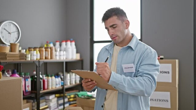 Radiant young hispanic chap volunteering at a charity center - confidently documenting donations