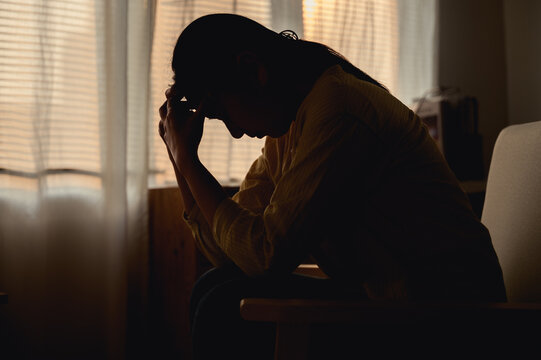 Silhouette photo of young Asian woman feeling upset, sad, unhappy or disappoint crying lonely in her room. Young people mental health care problem lifestyle concept.
