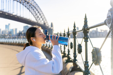 Asian woman in sportswear drinking water from a bottle after jogging exercise in the morning....