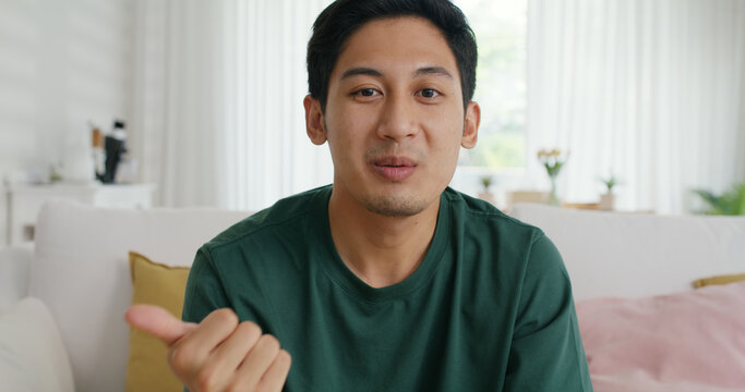 Young adult man Gen Z asia people sit relax happy remote work at home sofa couch video call online class smile look at webcam camera. MBA student vlogger guy record live vlog on social media screen.