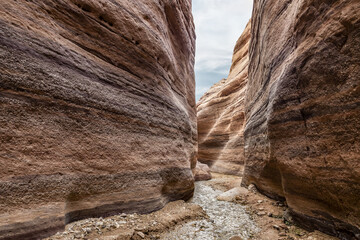 A small  shallow stream flows between high rocks with beautiful natural patterns on their walls at end of walking trail in the Wadi Numeira gorge in Jordan