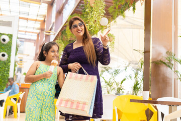 Happy indian Mother point aside daughter enjoying in shopping mall with shopping bag in mother hand...