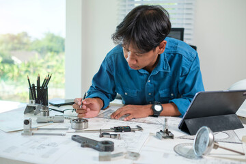 Adult male engineer working with blueprints and mechanical parts at office.