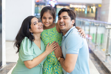 Happy indian family of three enjoying and embracing their daughter in shopping mall. Shopping...