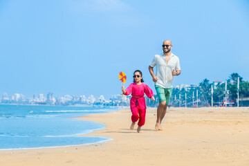 Indian father and daughter running on tropical beach and enjoying summer vacation. daughter playing...