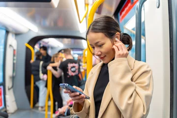  Asian woman using mobile phone and listening to the music on earphones during travel on tram in the city. Attractive girl enjoy urban lifestyle in the city with using wireless technology on device. © CandyRetriever 