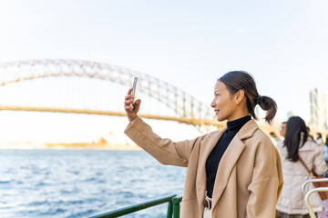 Asian woman using mobile phone taking selfie during travel on ferry boat crossing harbor in Sydney,...