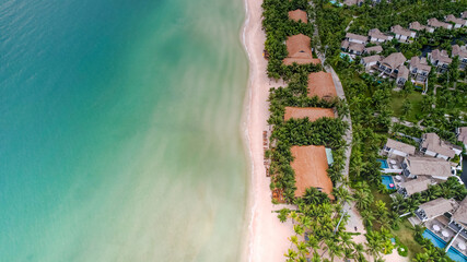Aerial view of a tropical beach with clear blue waters, sandy shoreline, palm trees, and luxury resort villas, illustrating a vacation or travel concept