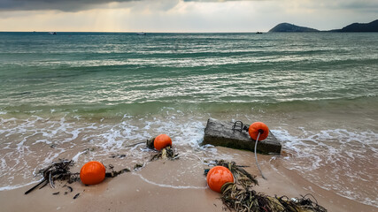 Buoy and rope washed up on a sandy beach with waves and a cloudy sky, depicting ocean debris or beach scenery - obrazy, fototapety, plakaty