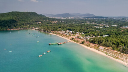 Aerial view of a tranquil tropical coastline with boats, clear turquoise water, and lush greenery, depicting a serene beach destination
