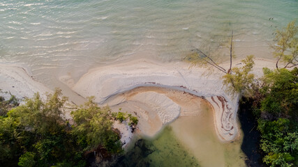 Aerial view of a serene tropical beach with gentle waves, surrounded by lush greenery, illustrating a tranquil vacation concept