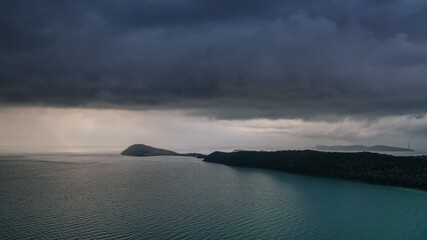 A serene seascape with overcast skies signaling an approaching storm over tranquil waters, featuring islands and a forested coastline