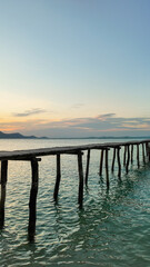 Obraz premium An old wooden pier stretches into calm sea waters with a tranquil sunset over the horizon, conveying a serene and peaceful concept