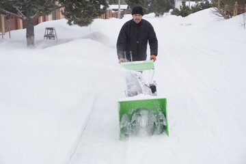 A man cleans snow in the winter in the courtyard of the house,  man cleaning snow with a snow blower
