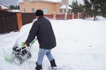 A man cleans snow in the winter in the courtyard of the house,  man cleaning snow with a snow blower