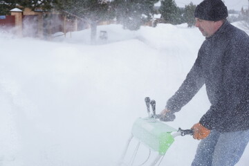 A man cleans snow in the winter in the courtyard of the house,  man cleaning snow with a snow blower