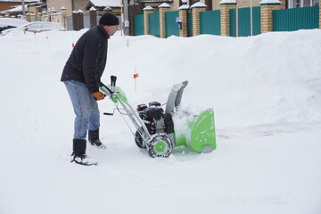 A man cleans snow in the winter in the courtyard of the house,  man cleaning snow with a snow blower