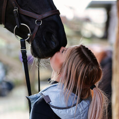 Girl blonde in blue quilted vest with ponytail plays with her horse, portraits of the woman with...