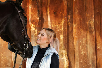 Girl blonde in blue quilted vest with ponytail plays with her horse, portraits of the woman with...