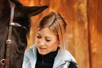 Girl blonde in blue quilted vest with ponytail plays with her horse, portraits of the woman with...