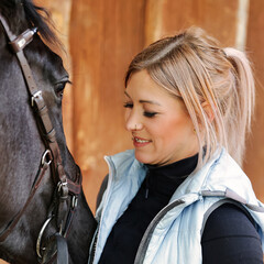 Girl blonde in blue quilted vest with ponytail plays with her horse, portraits of the woman with...