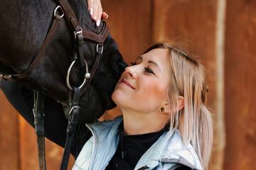 Girl blonde in blue quilted vest with ponytail plays with her horse, portraits of the woman with...