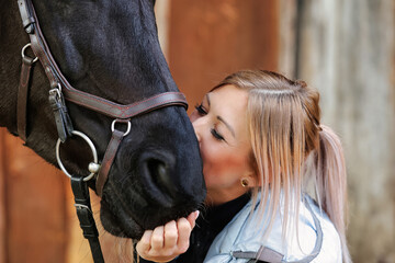 Girl blonde in blue quilted vest with ponytail plays with her horse, portraits of the woman with...