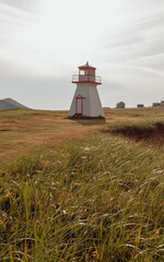 vue sur un phare blanc et rouge avec du gazon vert lors d'une soirée d'été au coucher de soleil