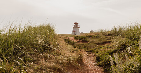 vue sur un phare rouge et blanc en bord de mer avec du gazon vert en été et un chemin en avant plan