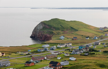 vue sur une falaise de roche en bord de mer avec du gazon vert ainsi que des maisons et une route en été