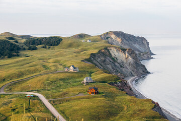 vue sur une falaise de roche grise en bord de mer avec du gazon vert ainsi que des maisons et une route en été