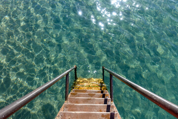 The wooden steps of the pier descend into clear blue water. Pier in the sea. Turquoise background