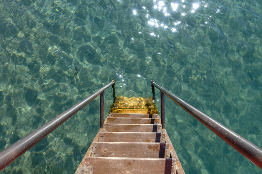 The wooden steps of the pier descend into clear blue water. Pier in the sea. Turquoise background