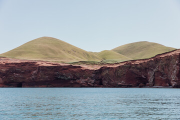 vue sur une falaise en roche rouge et des collines recouvertes de gazon sur le dessus au bord de l'eau en été lors d'une journée ensoleillée