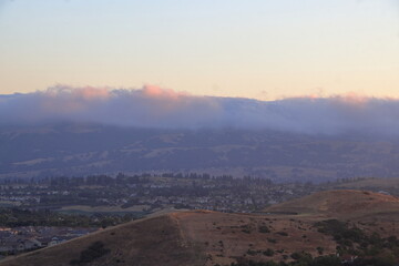 Fototapeta na wymiar The Marine layer moves in the East Bay at sunset as the hilltops and clouds lit up in a golden hue of the setting sun