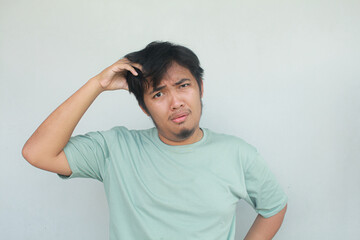 Asian young man with confused expression and feeling dizzy with messy hair. isolated in gray...