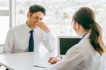 病院で女医に問診を受ける男性ビジネスマン（人間ドック・診断・診察）
