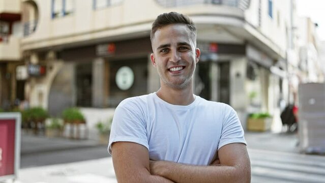 A handsome young man in a white t-shirt poses confidently on a vibrant urban street, exuding charm and casual style.