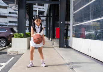 asian child or kid girl fun playing basketball and smile training to learning bouncing and raising ball alone at sports stadium school or basketball court for exercise on sport day and holiday