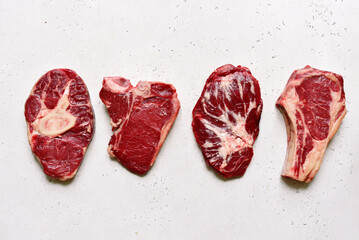 Different types of raw marbled beef steaks : T-bone, ossobuko, spider and rib eye with cleaver. Top...