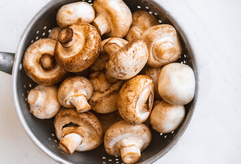 Raw mushrooms in an iron bowl on a white wooden background