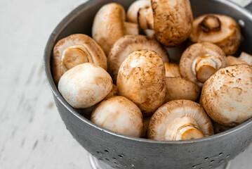 Raw mushrooms in an iron bowl on a white wooden background