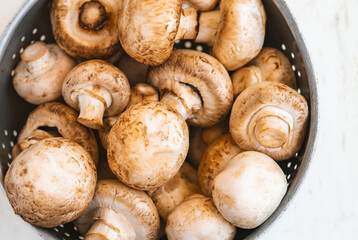 Raw mushrooms in an iron bowl on a white wooden background