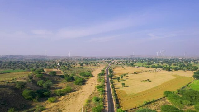 Aerial drone shot gaining height over road leading to windmill wind turbine generators in Jaisalmer Rajasthan Gujarat showing alternate renewable energy sources in thar desert and aravalli range
